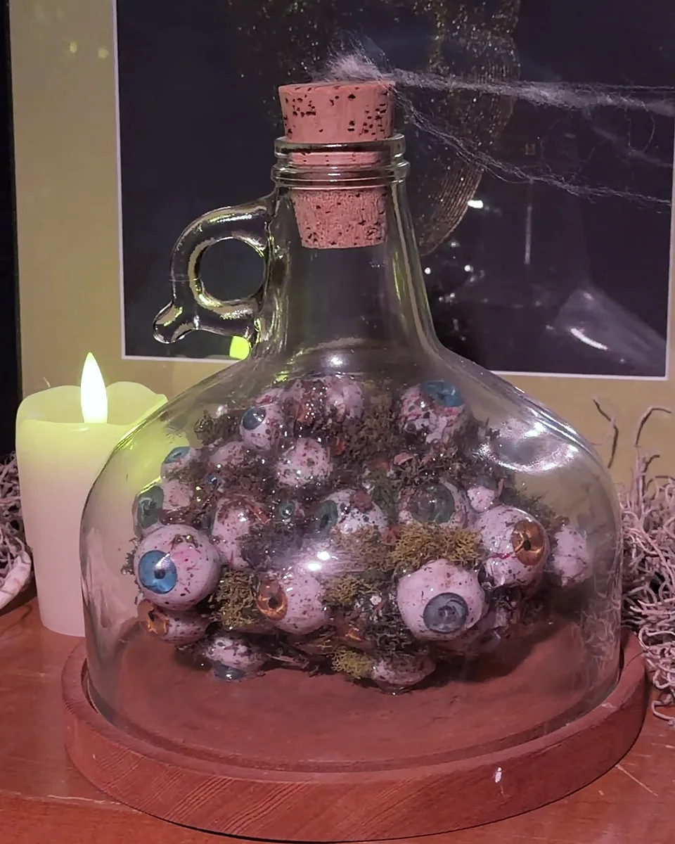 A corked glass jug packed with glass eyeballs, a candle beside it